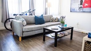 Un salon avec un canapé gris, une table basse noire, un vélo et une lampe.