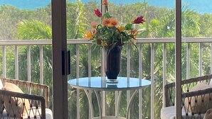 En balkon med et glasbord og stole, en vase med blomster og havudsigt.