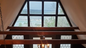 Une pièce dotée d’une grande fenêtre donnant sur un plan d’eau et des collines. On y trouve un ventilateur de plafond et un luminaire suspendu.