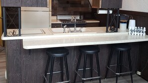 Une cuisine dotée d’un îlot central, de trois tabourets de bar noirs et d’un plancher en bois.