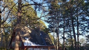 Une cabane dont le toit est recouvert de neige, entourée de grands pins et dotée d’une terrasse en bois.