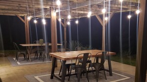 Une terrasse extérieure avec une table et des chaises en bois, des guirlandes lumineuses et un sol en béton.