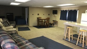 Ein Wohnzimmer mit einer Couch, einem Esstisch mit Stühlen, einem an der Wand montierten Fernseher und einer kleinen Küchenzeile mit Barhocker.