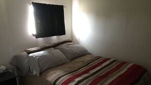 Ein Einzelbett mit gestreifter Bettdecke, ein Nachttisch und ein Wandvorhang.