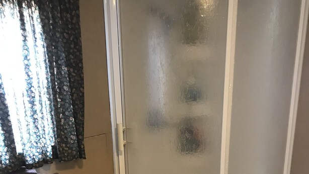 Eine Eckdusche mit Milchglas-Türen, ein Korbwäscheschrank auf einem Regal und ein gefliester Boden.