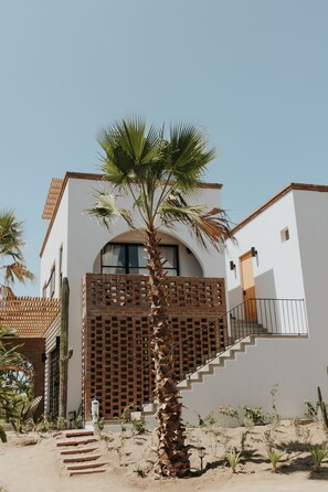A modern building with a white facade, a brick staircase, and a palm tree in the foreground. - Hotel So Far So Good (El Pescadero)
