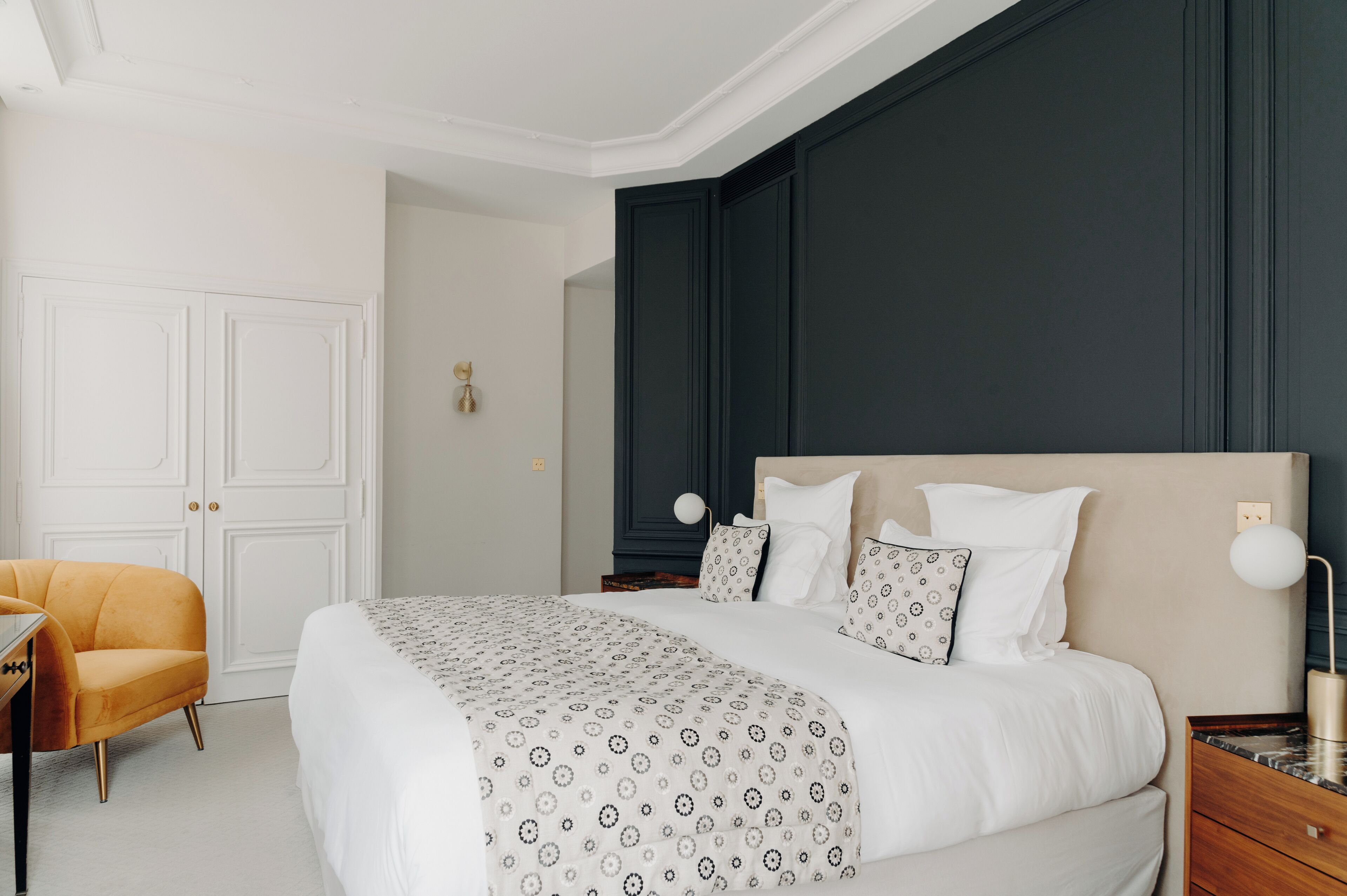 A neatly arranged bedroom with a large bed, a bedside table, a chair, and a wardrobe.