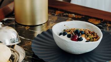 Een ontbijtsetting met een kom yoghurt en granola, een bord met toast en een decoratieve lamp op een marmeren tafel.
