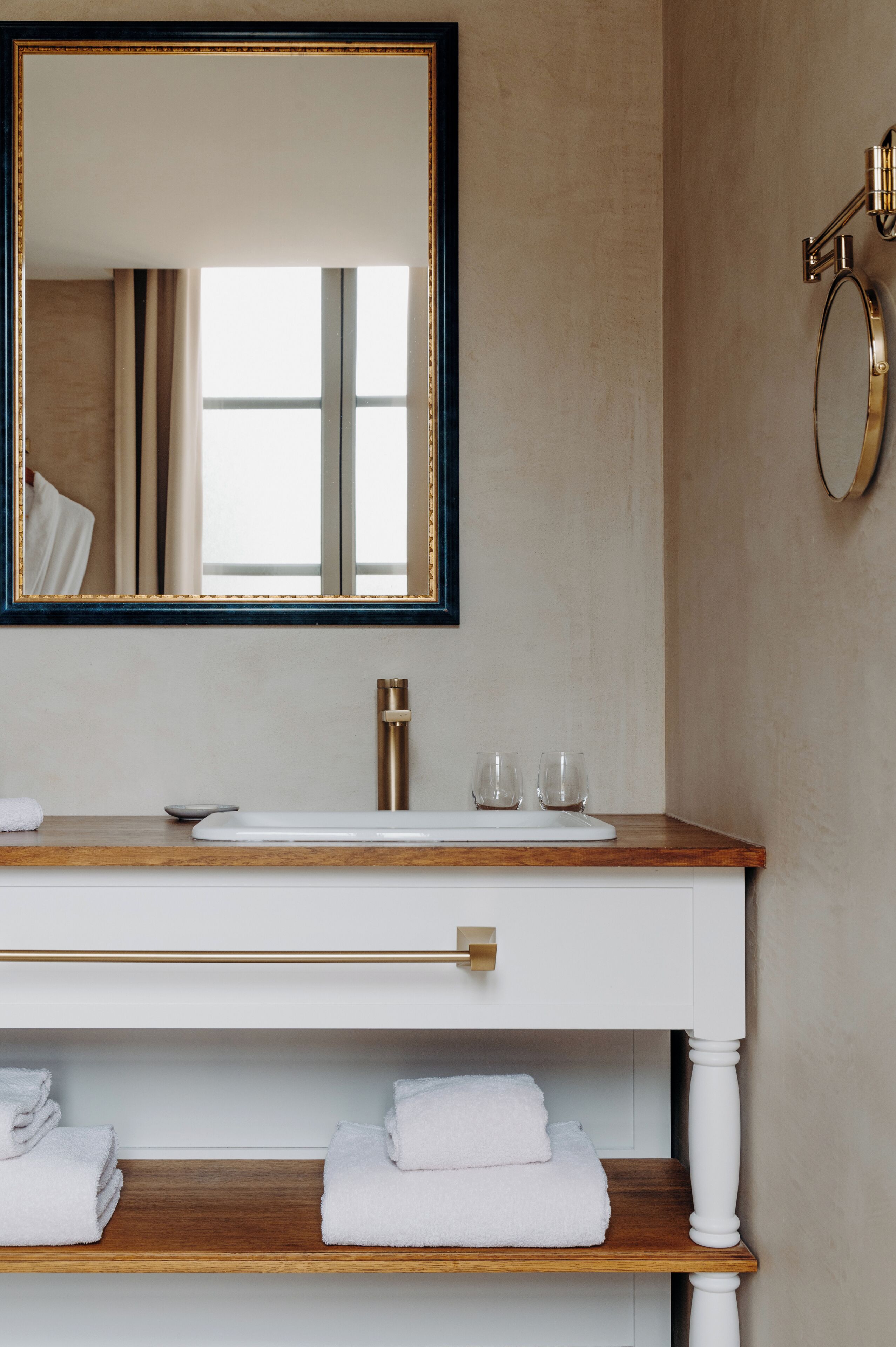 Une salle de bain avec un meuble-lavabo en bois, un grand miroir, un robinet doré et deux serviettes posées sur une étagère.