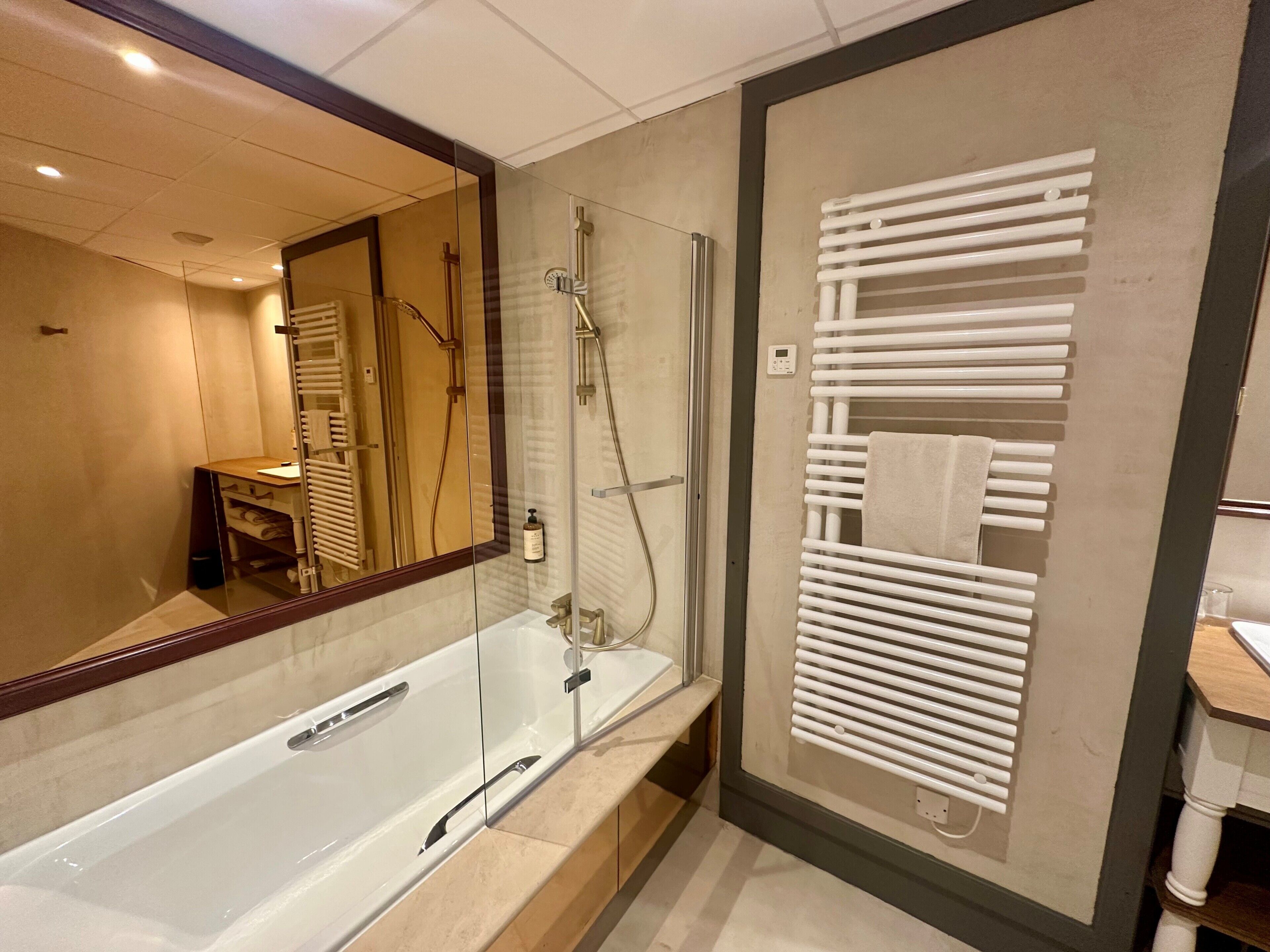 A modern bathroom with a glass-enclosed shower, a large mirror, and a towel rack.