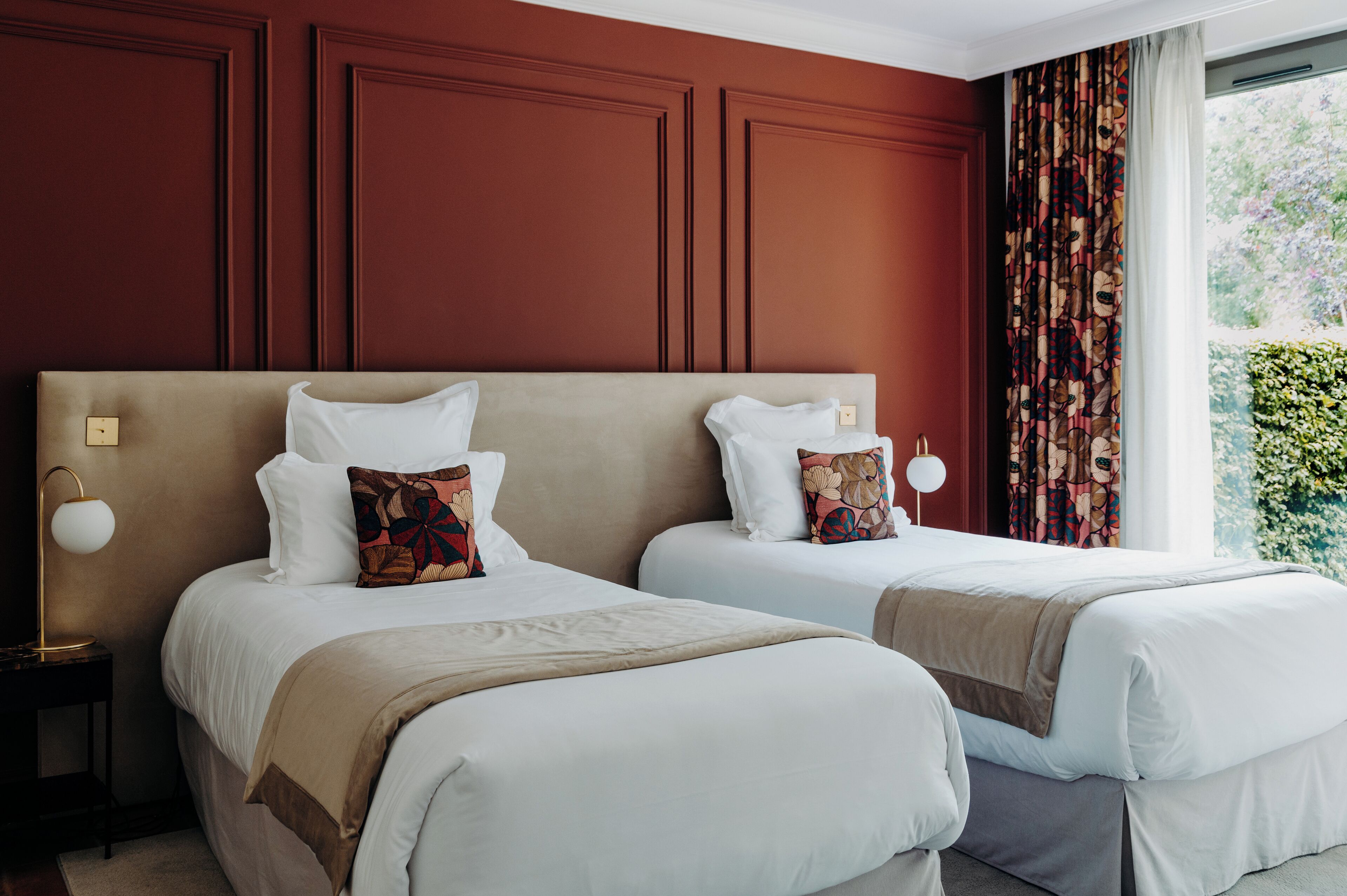 A hotel room with two beds, a large window with curtains, and a nightstand with a lamp.