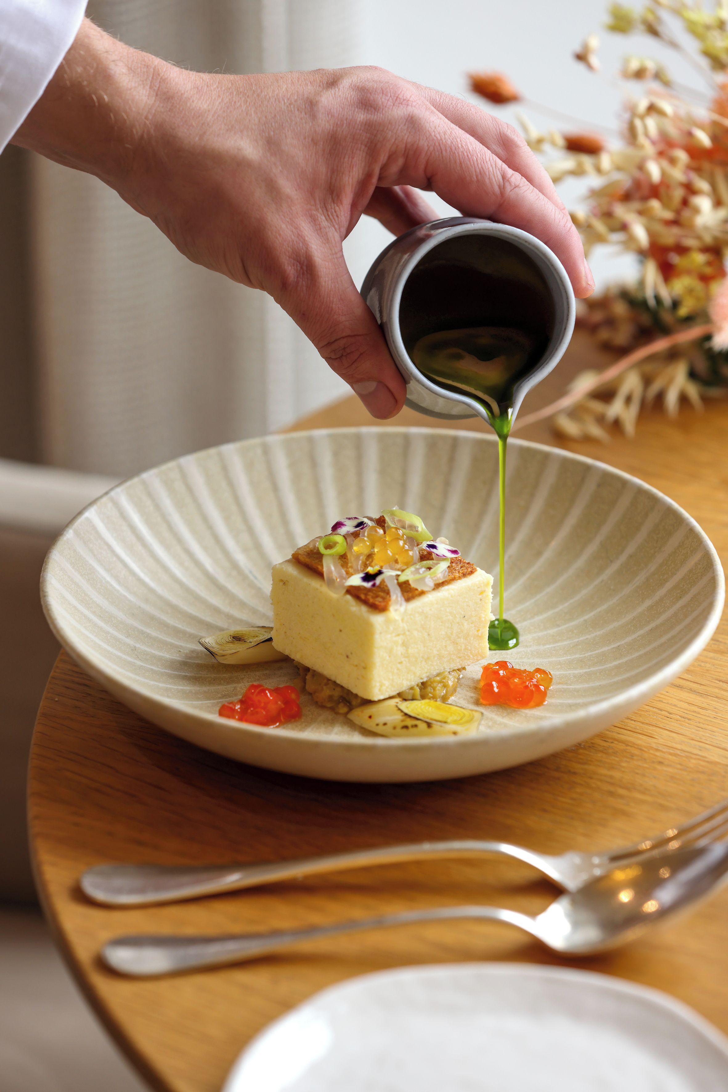 Una mano vertiendo una salsa verde sobre un postre en un plato.