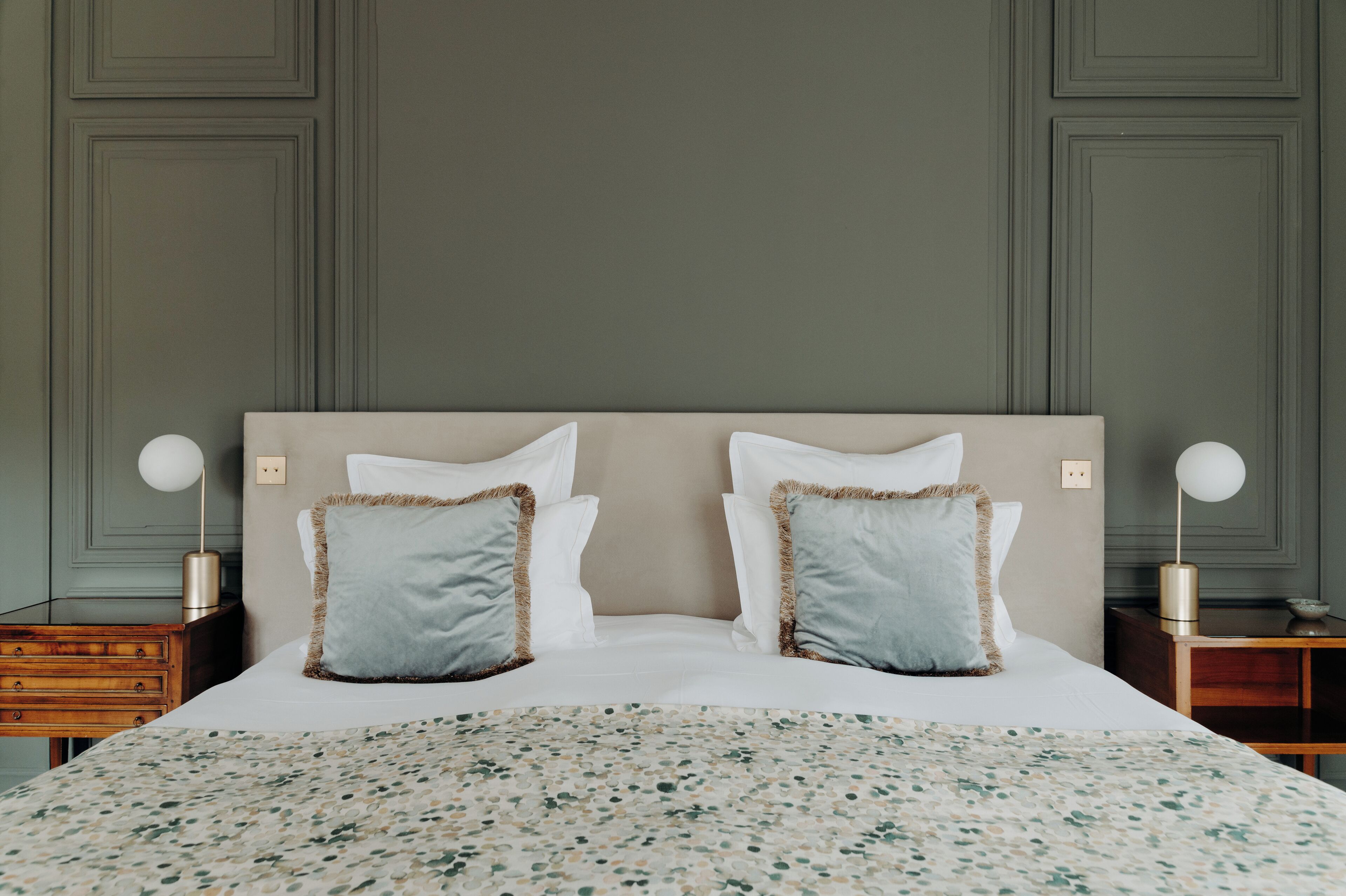 Una cama bien hecha con una colcha estampada con motivos florales, dos almohadas a juego y dos lámparas de noche sobre mesitas de madera.