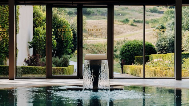 Una piscina con fuente, rodeada por amplios ventanales que ofrecen vistas a un jardín paisajístico.
