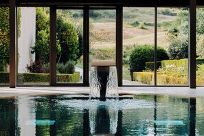 Una piscina con fuente, rodeada por amplios ventanales que ofrecen vistas a un jardín paisajístico.