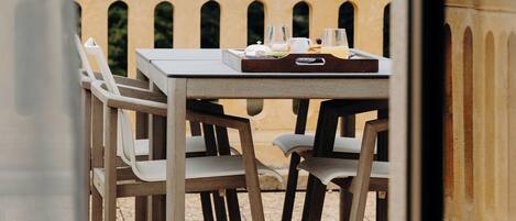 Un espacio para comer al aire libre con una mesa, sillas, un vaso de agua y un plato de comida.