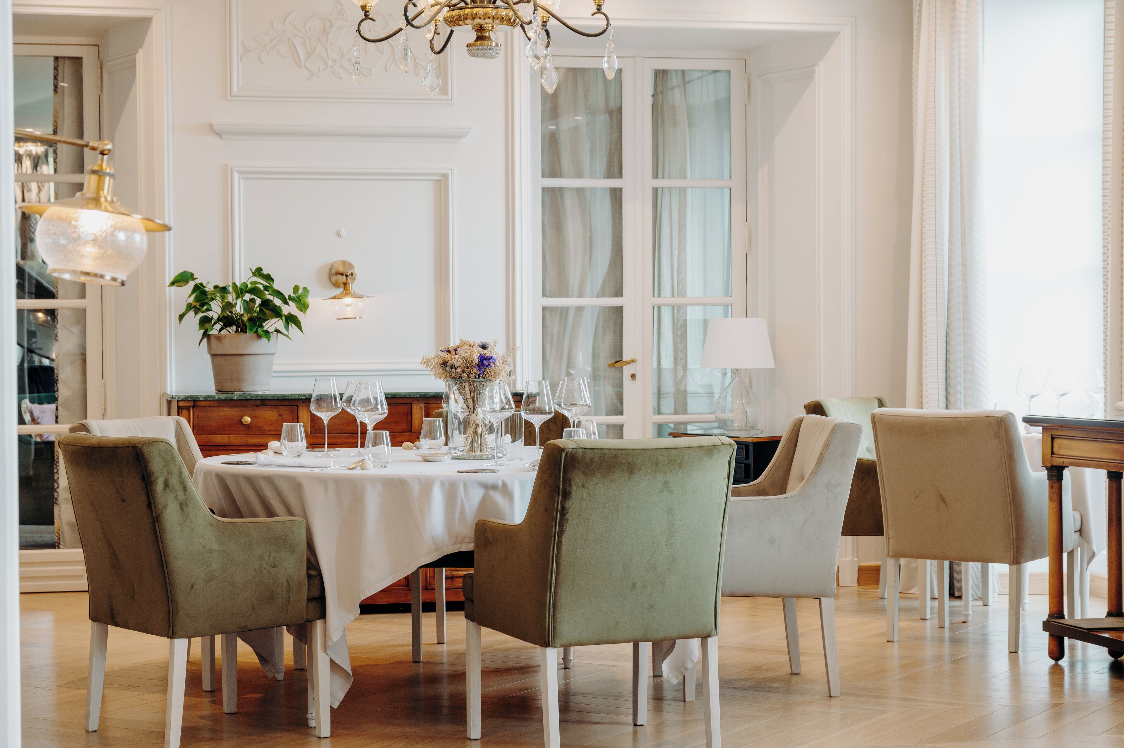 Un comedor con una mesa dispuesta para cuatro personas, rodeada de sillas, una araña y una planta en maceta.
