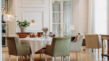 Un comedor con una mesa dispuesta para cuatro personas, rodeada de sillas, una araña y una planta en maceta.