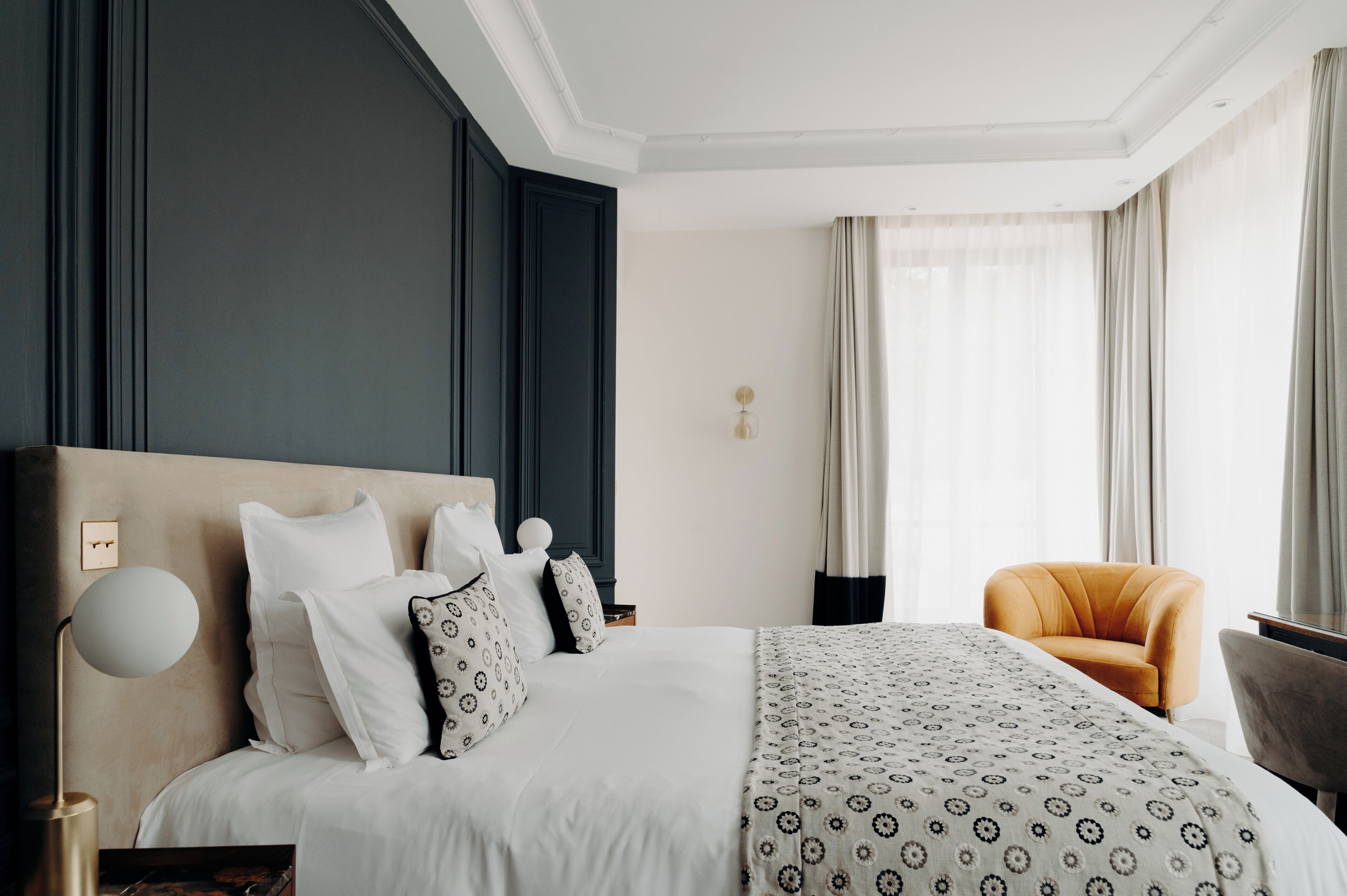 Habitación de hotel con una cama grande, una mesita de noche, una lámpara, una silla y una ventana con cortinas.