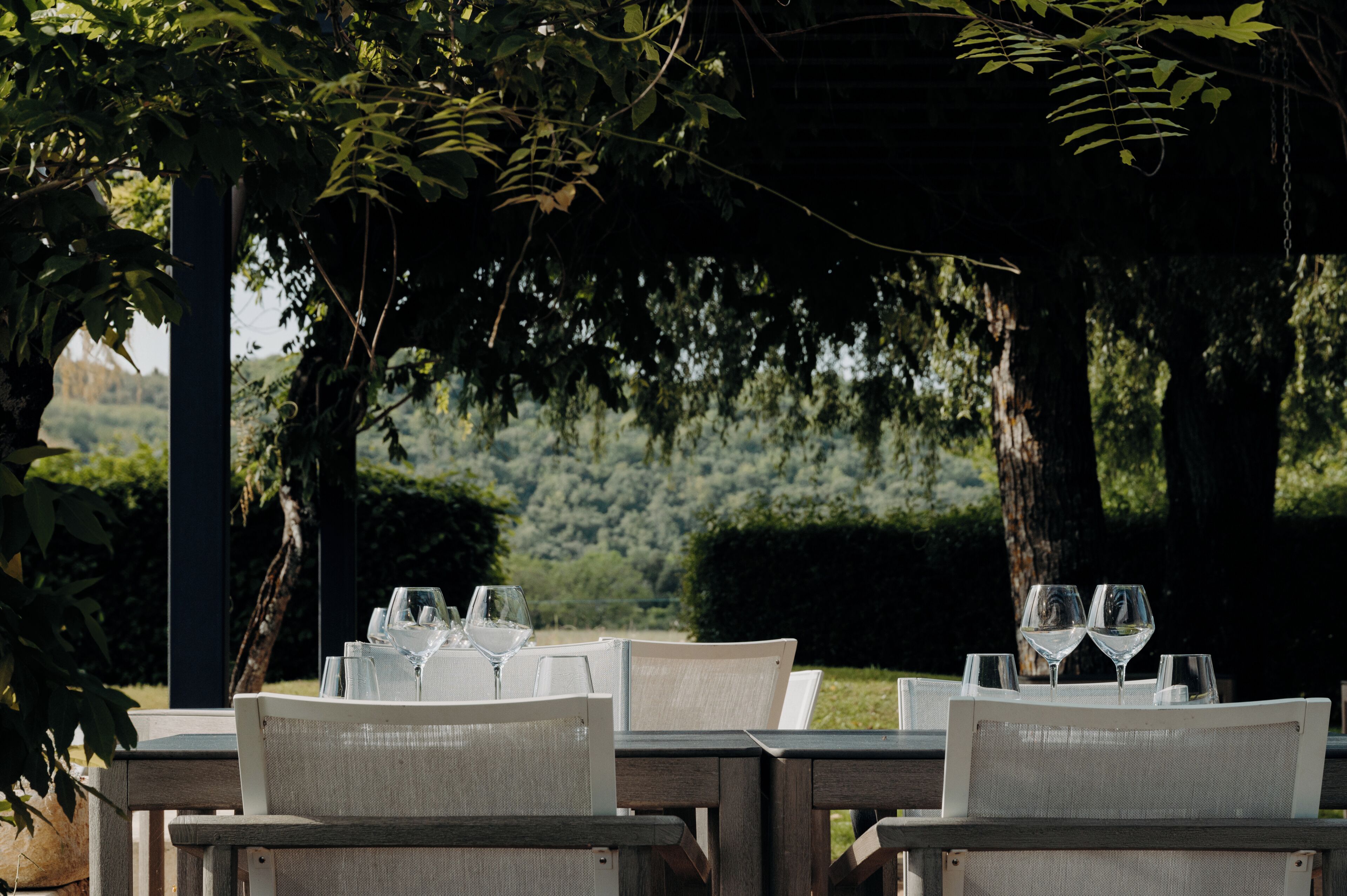 An outdoor dining area with a table set for two, surrounded by chairs, and overlooking a forested landscape.