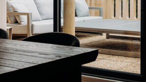 Una terraza con vistas a una colina boscosa, que incluye una mesa de madera y un sofá con cojines.