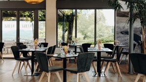 Un restaurante con amplios ventanales, sillas negras y mesas de madera dispuestas para comer.