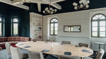 Un salón de conferencias con una amplia mesa de madera, asientos cómodos y una lámpara de araña moderna.