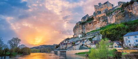A historic castle on a cliff overlooking a river, with a bridge connecting to the town below.