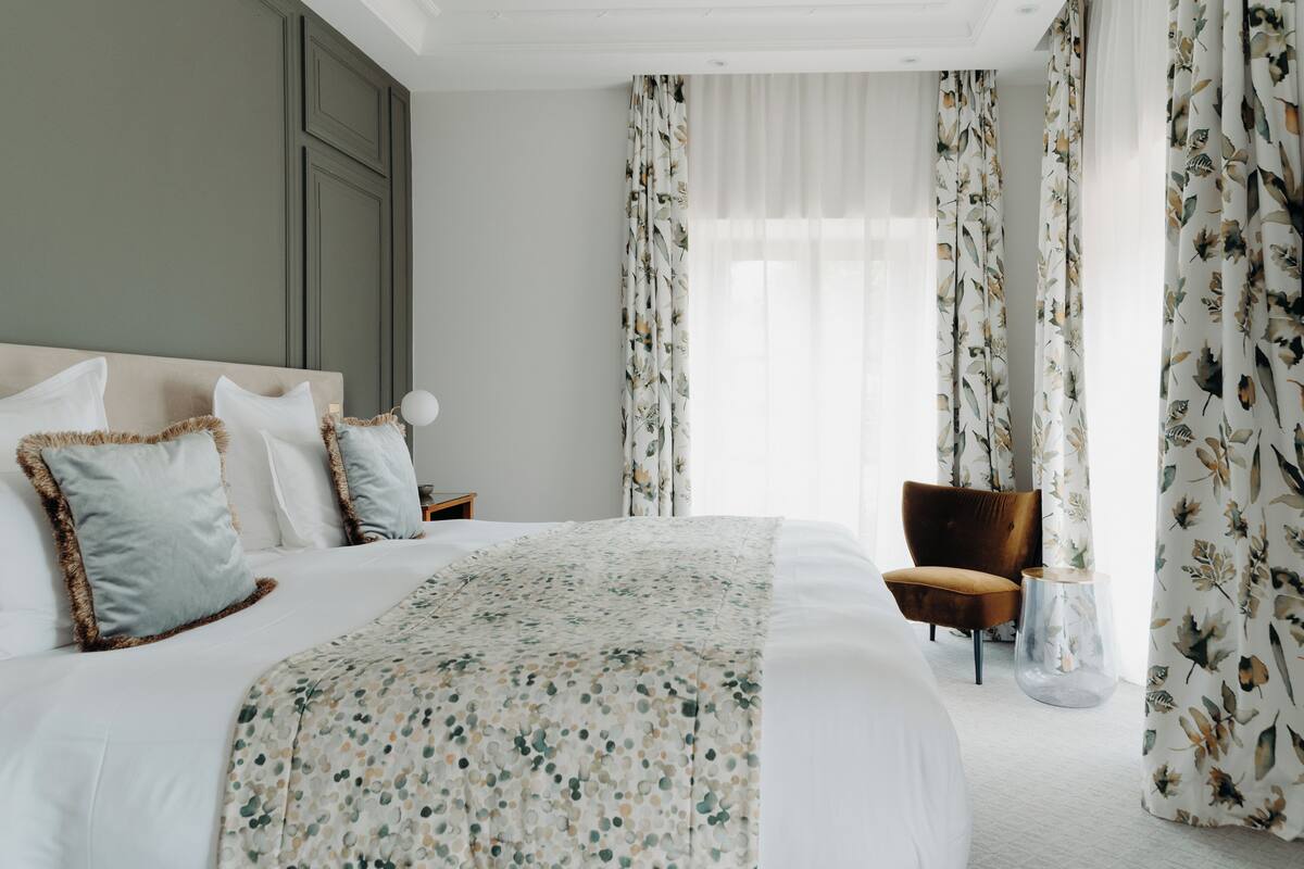 Une chambre d’hôtel avec un grand lit, une table de chevet en bois, une chaise et une petite table sur laquelle se trouve un vase.