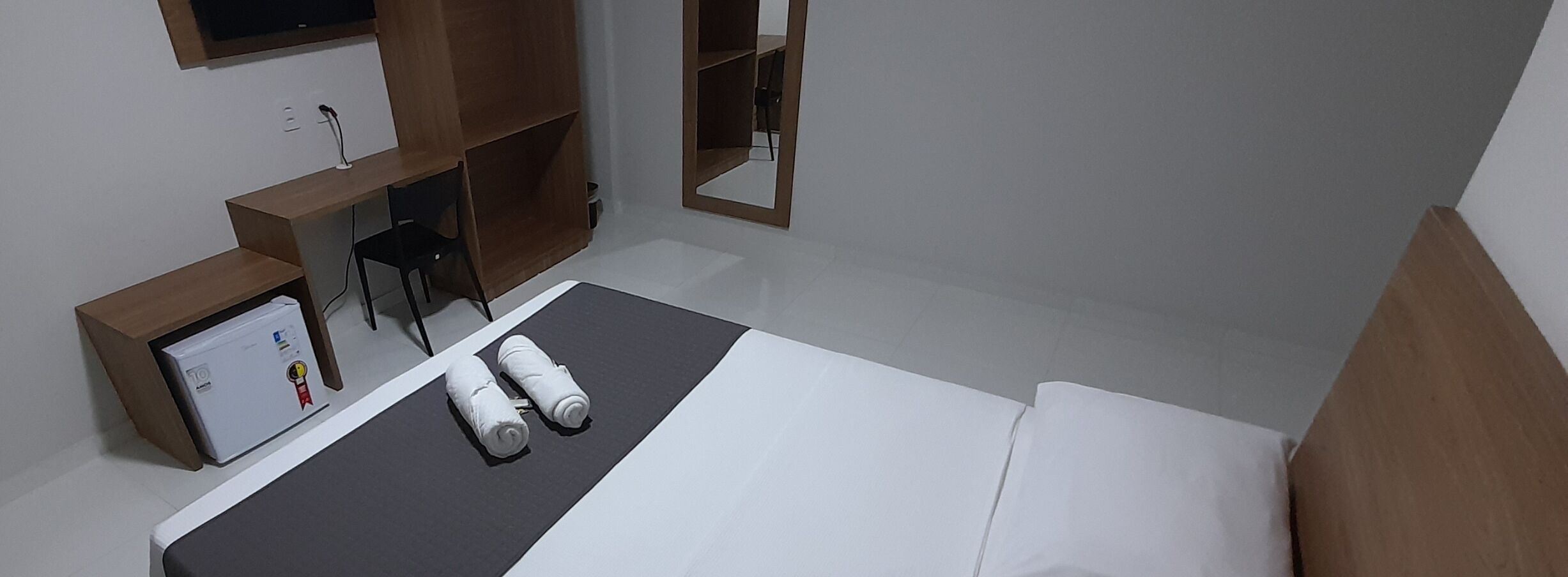 A hotel room with a bed, a desk, a chair, and a small refrigerator.