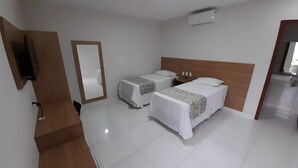 Une chambre d’hôtel avec deux lits simples, une tête de lit en bois, un téléviseur à écran plat, un miroir et un appareil de climatisation blanc.