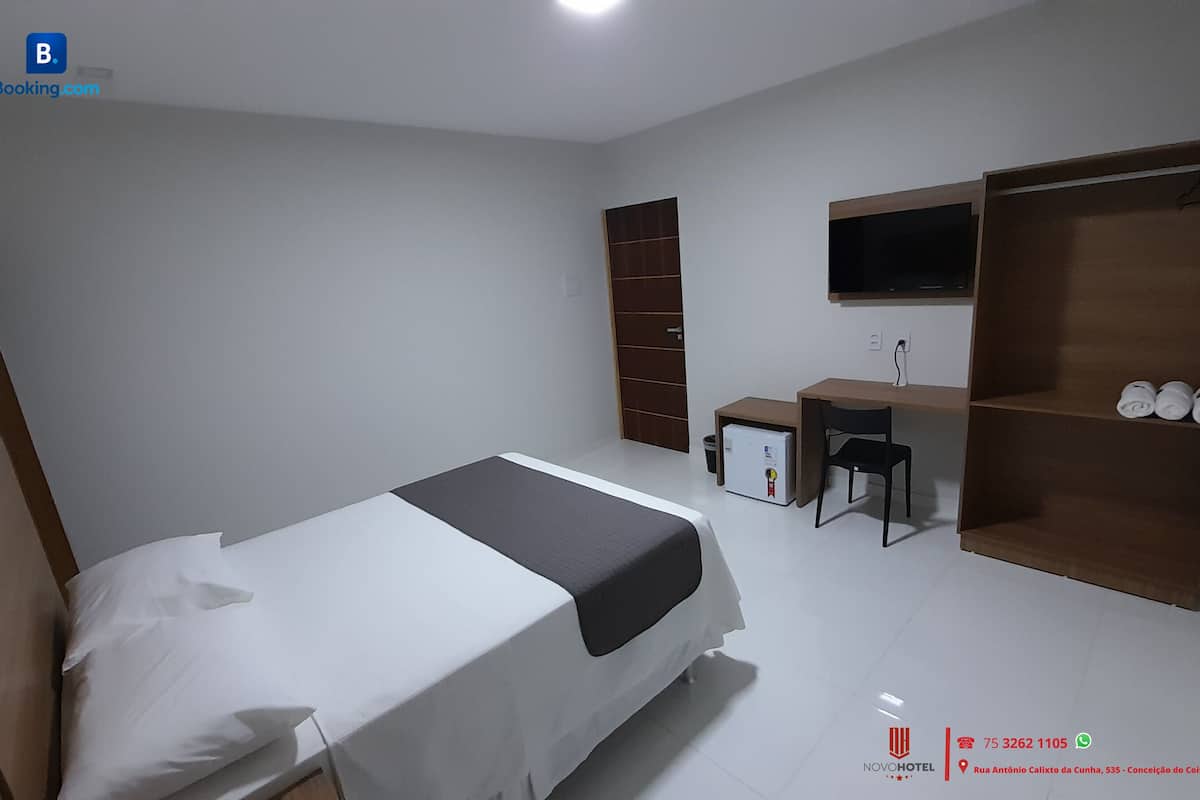 A hotel room with a single bed, a desk, a chair, a wardrobe, and a television.