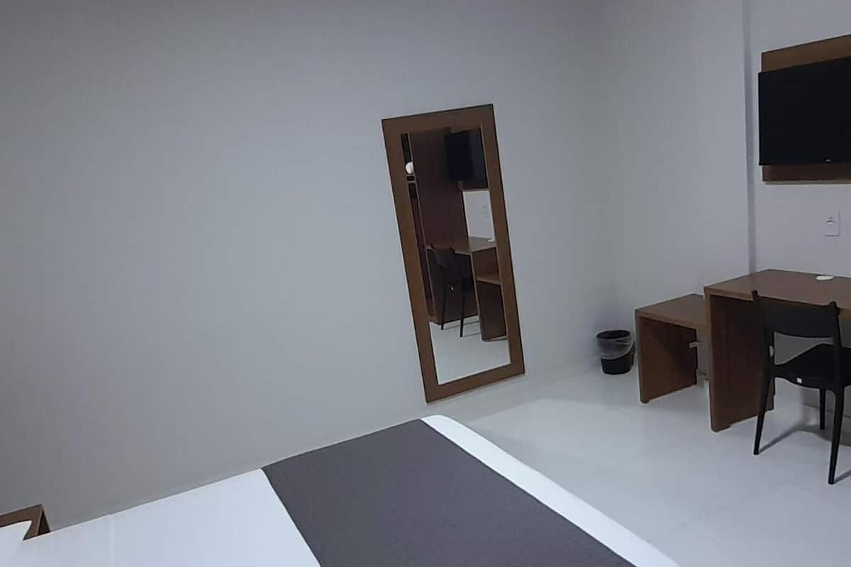 A bedroom with a bed, a desk, a chair, a wardrobe, and a mirror.