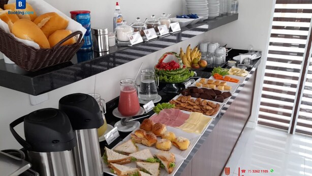 Un buffet proposant une variété d’aliments, notamment des sandwichs, des fruits et des boissons. Des condiments et une machine à café sont également à disposition.