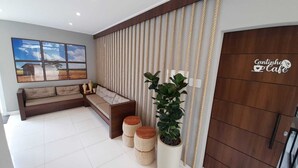Un salon moderne avec un canapé d’angle, une grande plante en pot et une porte en bois ornée d’un logo.