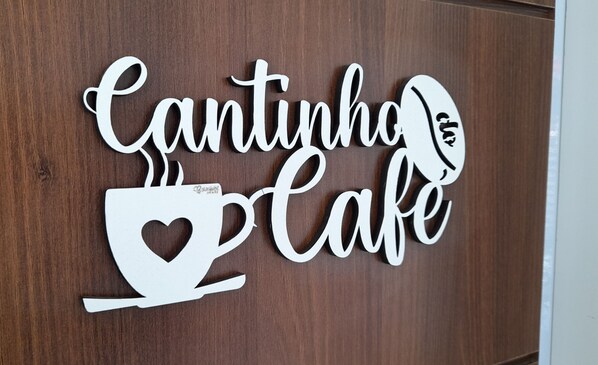 Decoración de pared con el texto "Cantinho Cafe" y una taza humeante.