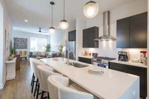 A modern kitchen with a large island, dark cabinetry, and pendant lighting.