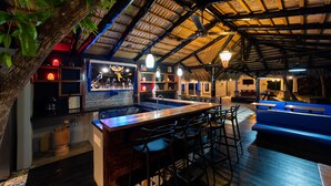 Un área de bar interior con barra de madera, taburetes y mesa de billar.