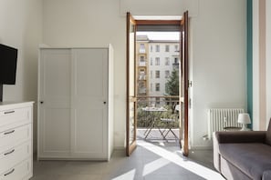 A room with a sliding door leading to a balcony, a white wardrobe, a sofa, and a radiator.