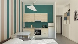A compact room with a bed, a small table, a chair, a kitchenette, and a ceiling light. - Hostmate - Milano - Botticelli - Città Studi  (Milano)