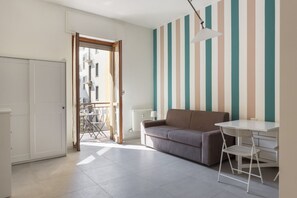 Um quarto com sofá, mesa, cadeira, radiador, porta e janela.