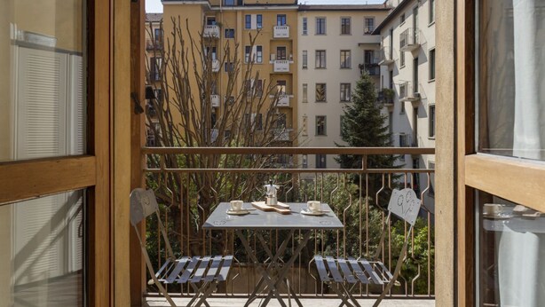 A balcony with a table and chairs, a view of buildings, and a tree. - Hostmate - Milano - Botticelli - Città Studi  (Milano)