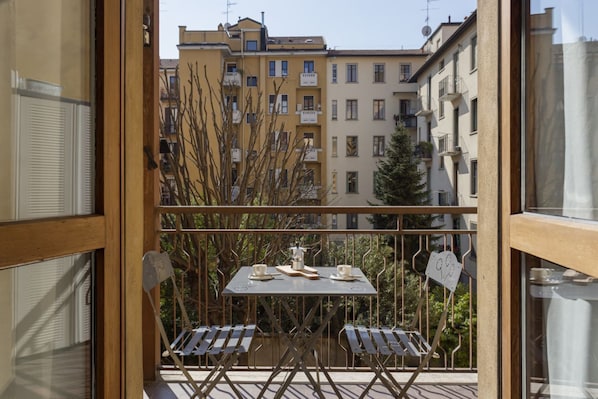 A balcony with a table and chairs, a view of buildings, and a tree.