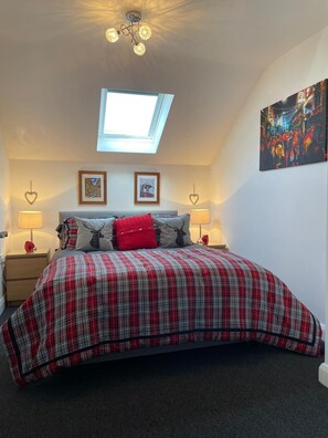 A bedroom with a skylight, a bed with a plaid bedspread, two framed pictures, and two bedside lamps. - The Glynn, Portrush. Deluxe holiday home, 8 beds 12 guests 5 bedrooms. (Portrush)