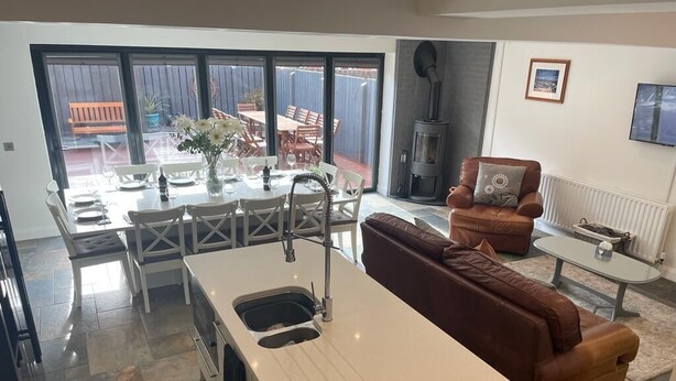 Een moderne keuken met een centraal eiland, een eethoek met tafel en stoelen, een gezellige bruine bank en een open haard.
