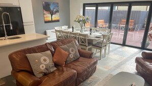 Een woonkamer met een bruine leren bank, een bijzettafeltje en een eethoek met een tafel gedekt voor vier personen.