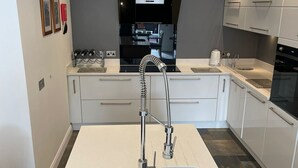 Een moderne keuken met een centraal eiland, roestvrijstalen apparatuur en een grijze spatwand.