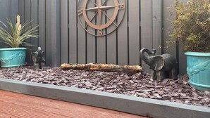 Een tuin met een decoratieve metalen kompas, twee potten met planten en een houten boomstam.