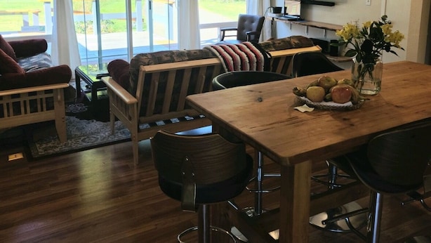 Un salon moderne avec une table à manger en bois, des tabourets de bar et un téléviseur fixé au mur.