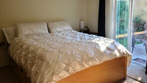 Une chambre avec un grand lit, une table de chevet, une lampe et une vue sur l’extérieur grâce à une porte-fenêtre coulissante.
